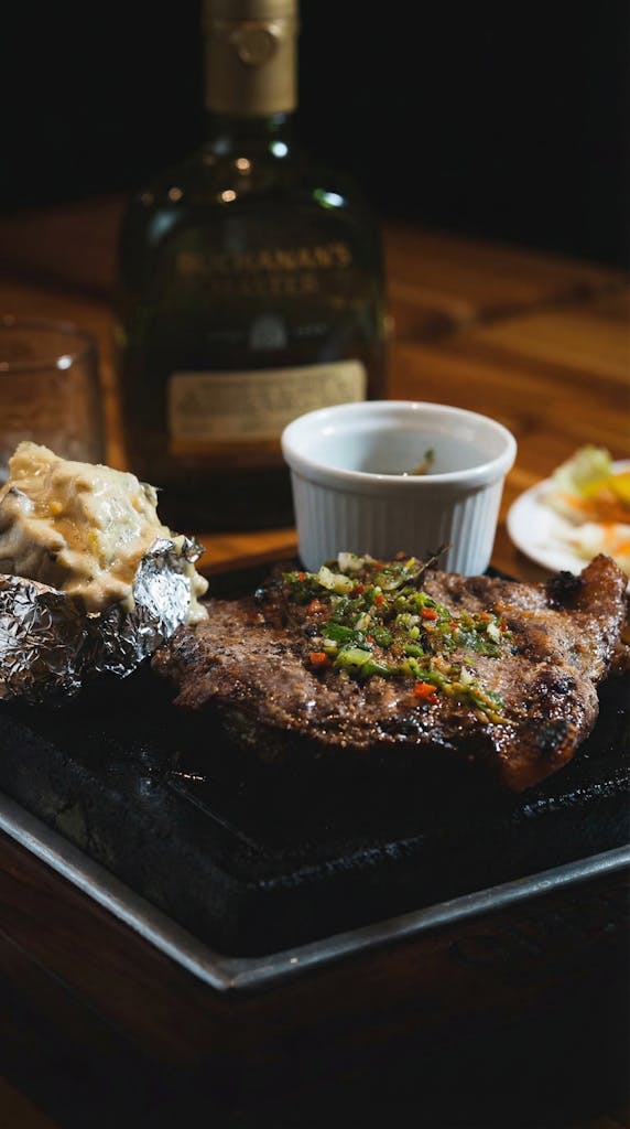 A delicious grilled steak with baked potato served with whisky, capturing the essence of Colombian cuisine.